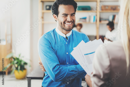Two coworkers making a great business project discussion in modern office.Successful confident hispanic businessman talking with young woman. Horizontal, blurred background.