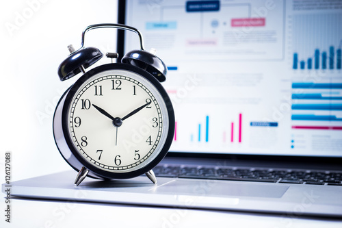 Clock alarm with stock graph chart in laptop screen background.