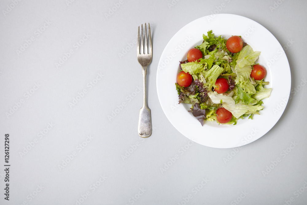Aerial view of a dish of classic side salad on a pastel grey background with fork and blank space at side Aerial view of a dish of classic side salad on a pastel grey background with fork and blank space at side