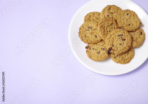 A plate full of freshly baked oatmeal and raisin cookies on a pastel purple background with blank space at side