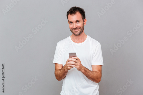 Happy uoung man holding smartphone and looking at camera photo