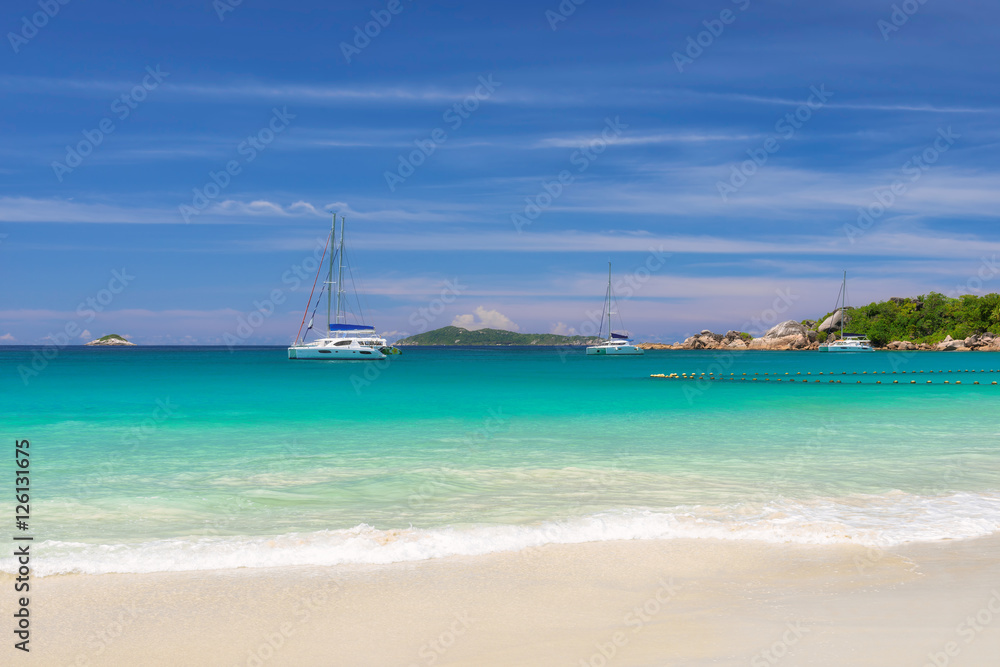 The sea is turquoise and yachts at anchor on tropical island. Fashion travel and tropical beach concept.