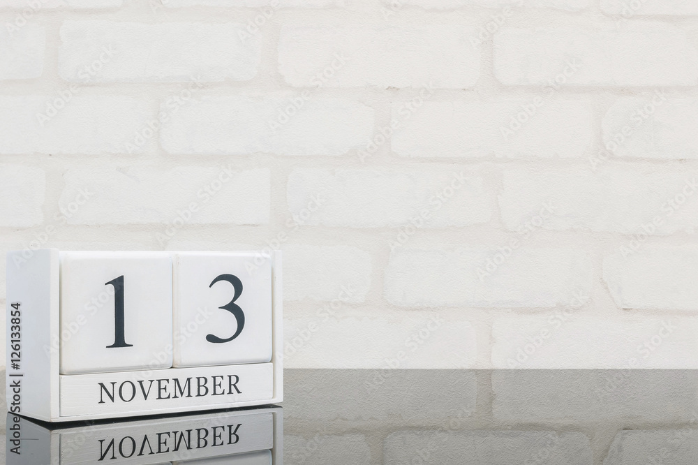 Obraz premium Closeup white wooden calendar with black 13 november word on black glass table and white brick wall textured background with copy space , selective focus at the calendar