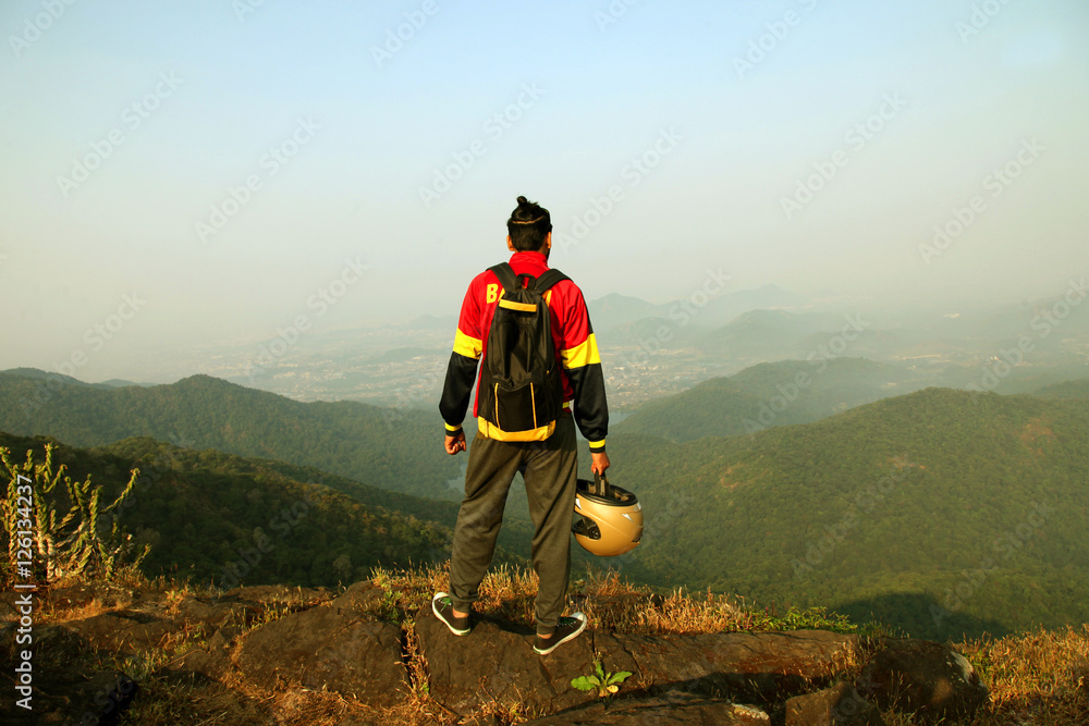 Obraz premium Young man with backpack and helmet standing on the top of a mountain and enjoying valley view