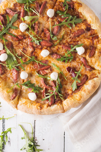 Thick-crust pizza with hunting sausages, mozzarella cheese on a white wooden background