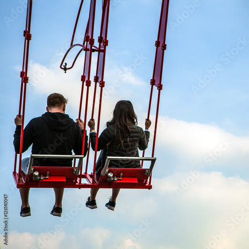 People having fun In swing carousel against blue sky.