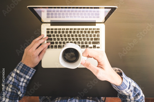 Male hands working on Laptop and holding a cup of coffee on the desk