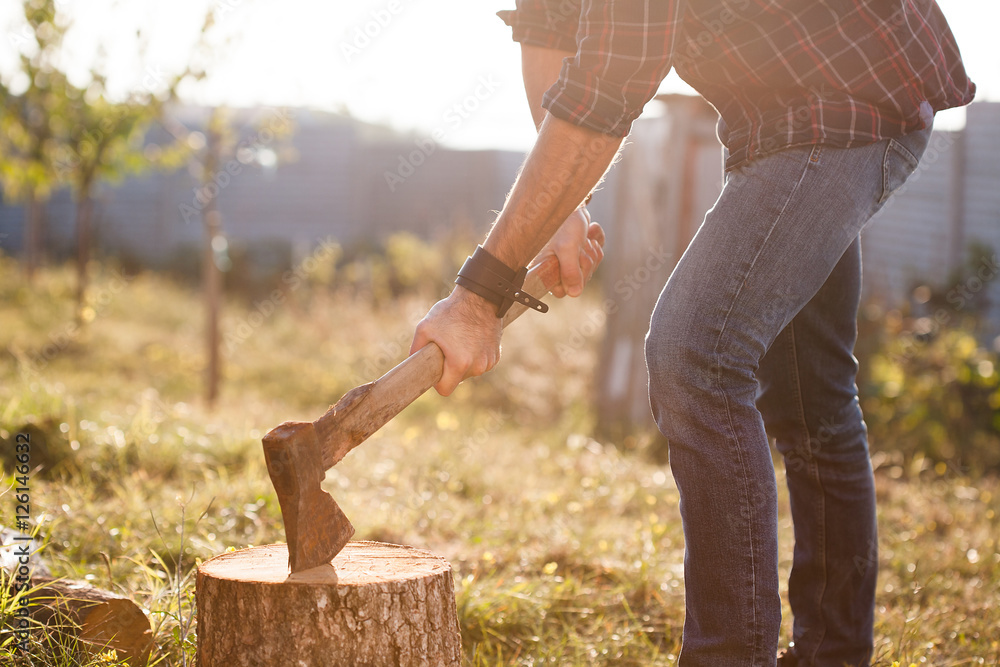 Man in jeans and checkered shirt chopping wood with axe