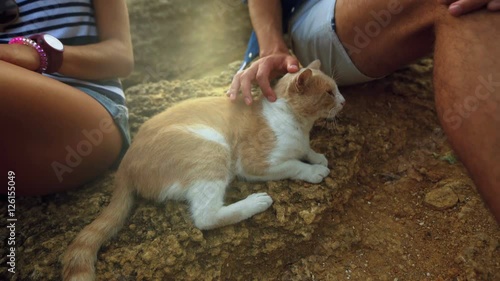 Close up of two young people sitting on the stone, man caressing red cat.