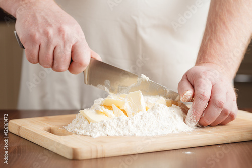 male hands pouring butter in flour to make dough
