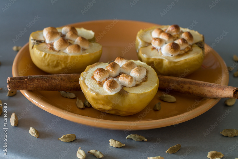 Appetizing baked apples with cottage cheese, cinnamon and marshmallows on orange plate. Decorated by cinnamon sticks and cardamom seeds.