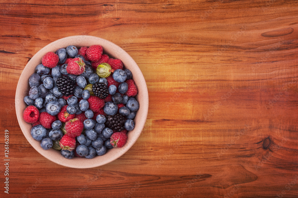 Brown ceramic plate with berries on the left of the wooden table with clipping path. Top view. Brown ceramic plate with berries on the left of the wooden table with clipping path. Top view.