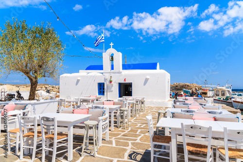 Taverna tables on square with typical white Greek church in Naoussa port, Paros island, Cyclades, Greece