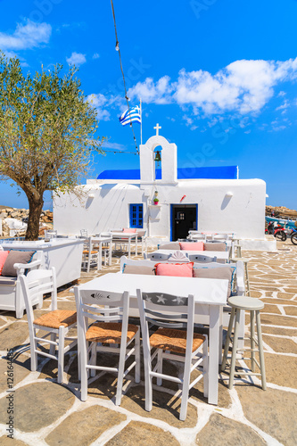 Fototapeta Naklejka Na Ścianę i Meble -  Taverna tables on square with typical white Greek church in Naoussa port, Paros island, Cyclades, Greece