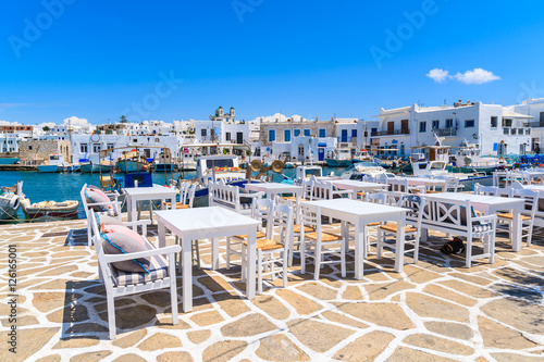 White taverna tables in Naoussa port with fishing boats, Paros island, Greece