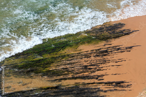 Rock formations on beach and surf wave.
