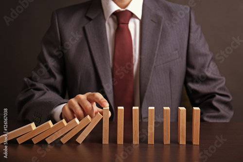 Фотография Businessman hand trying to stop toppling dominoes on table