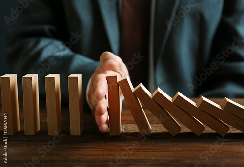 Businessman hand trying to stop toppling dominoes on table