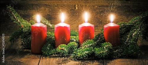 Vierter Advent: vier leuchtende Kerzen vor einem Holzhintergund