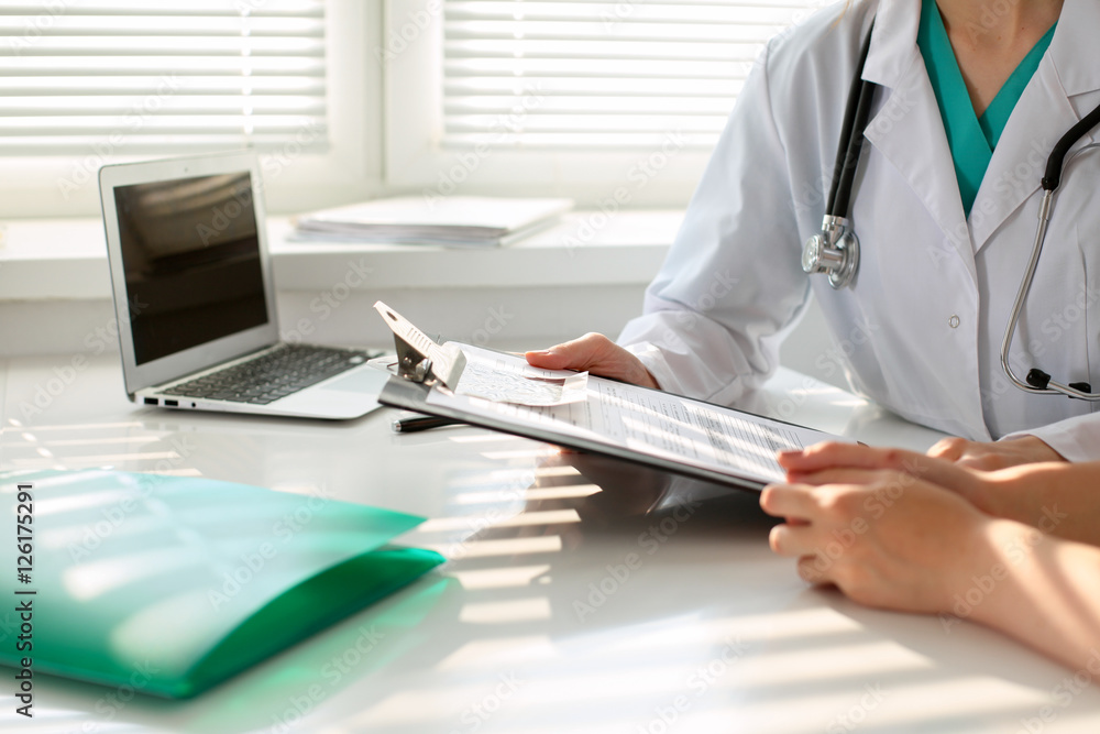 Fototapeta premium Doctor pointing into medical history form and discussing something with her patient. Close-up.