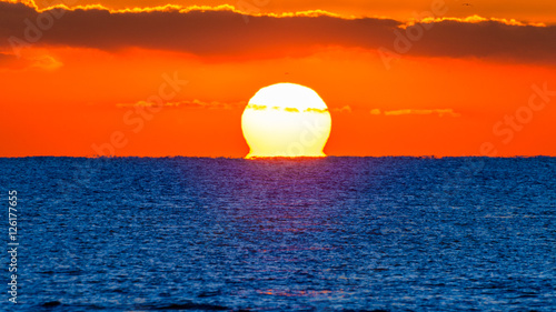 Fototapeta Naklejka Na Ścianę i Meble -  Amanecer del sol con el cielo naranja y el mar azul.