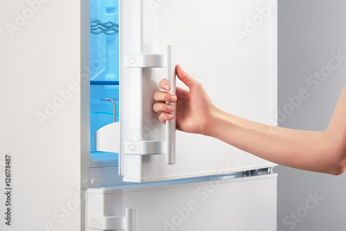 Female hand opening white refrigerator door on gray