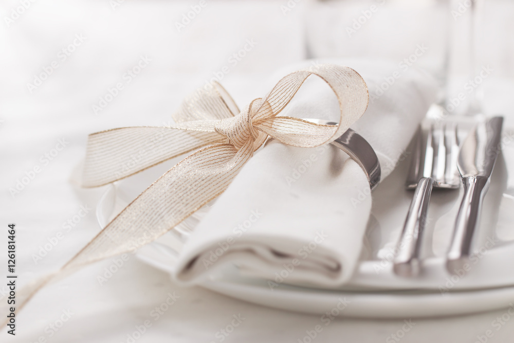 Beautifully elegant decorated table for holiday - wedding or valentine day with modern cutlery, bow, glass, candle and gift, closeup, toned Beautifully elegant decorated table for holiday - wedding or valentine day with modern cutlery, bow, glass, candle and gift, closeup, toned