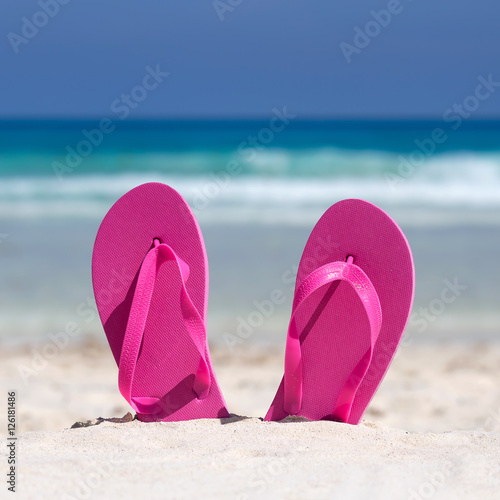 Pink flip flops on sandy beach near sea. Summer vacation concept