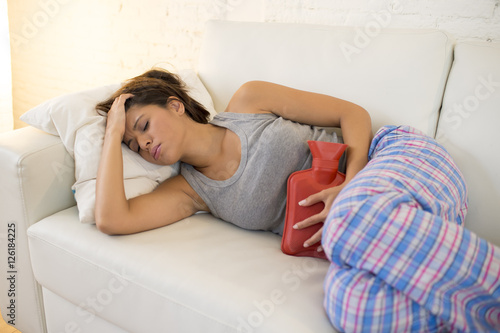 young beautiful hispanic woman holding hot water bottle against belly suffering menstrual period pain