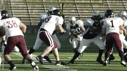 A quarterback hikes and hands off to a running back who runs downfield photo