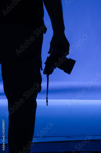 silhouette of a hand holding camera against blue background