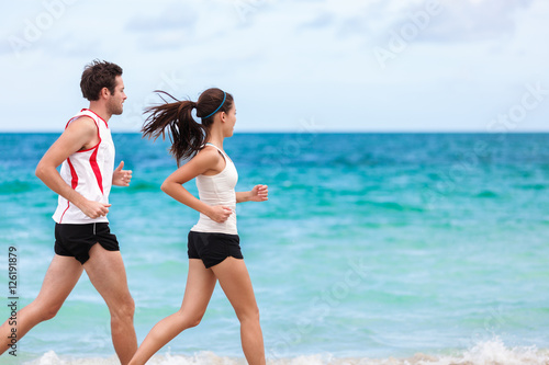 Fitness interracial couple runners running on beach. Running couple jogging together outside on ocean background. Athletes training cardio outdoors working out. Fit Asian woman, Caucasian man.