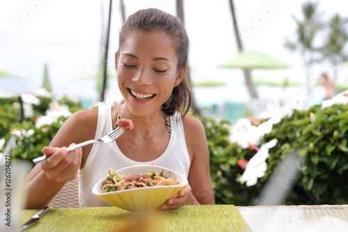 Asian woman eating a fresh raw tuna dish, hawaiian local food poke bowl, at outdoor restaurant table during summer travel vacation. Hawaii poke bowl food plate. Ahi tuna hawaiian cuisine.