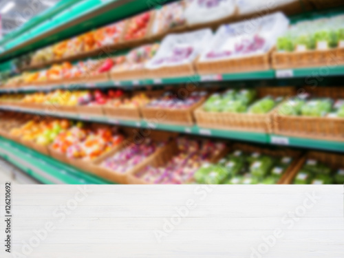 Wooden empty table in front of blurred supermarket vegetables shelf