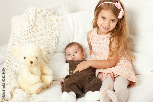 Adorable little child girl and boy sit in the bed with teddy bear
