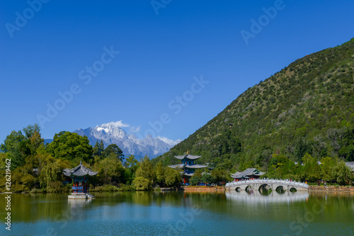 Black Dragon Pool to the Five Phoenix Tower and the Five Holes Bridge. In the background is Jade Dragon Snow Mountain. The Old Town of Lijiang is located in Lijiang City, Yunnan, China.