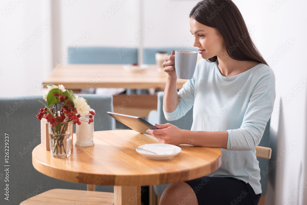 Joyful beautiful woman having a coffee and using her gadget. Joyful beautiful woman having a coffee and using her gadget.