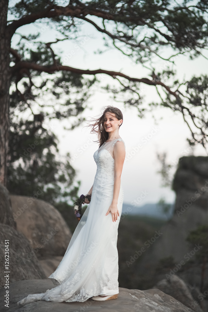 Gorgeous bride in elegant dress holding bouquet posing near forest 