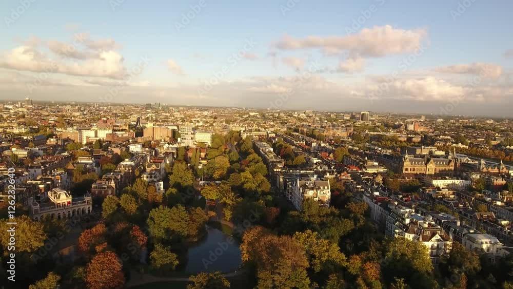 Aerial flying over Vondelpark towards Leidseplein in Amsterdam during golden hour. Beautiful view over the park with fall foliage and historic city center. Aerial flying over Vondelpark towards Leidseplein in Amsterdam during golden hour. Beautiful view over the park with fall foliage and historic city center.