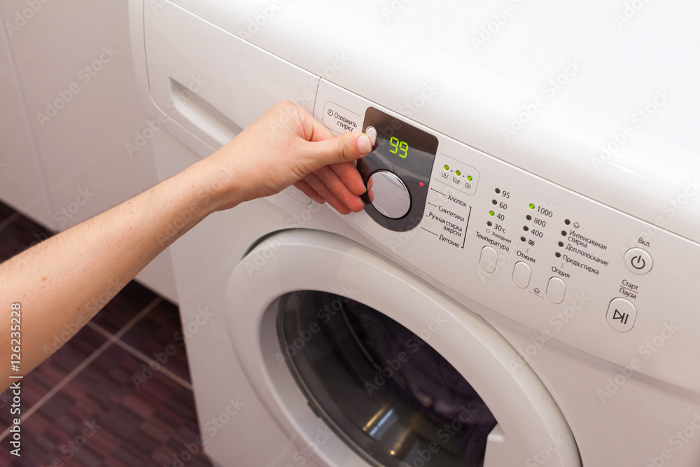 Young woman or housekeeper has a laundry day at home, she select the program Young woman or housekeeper has a laundry day at home, she select the program
