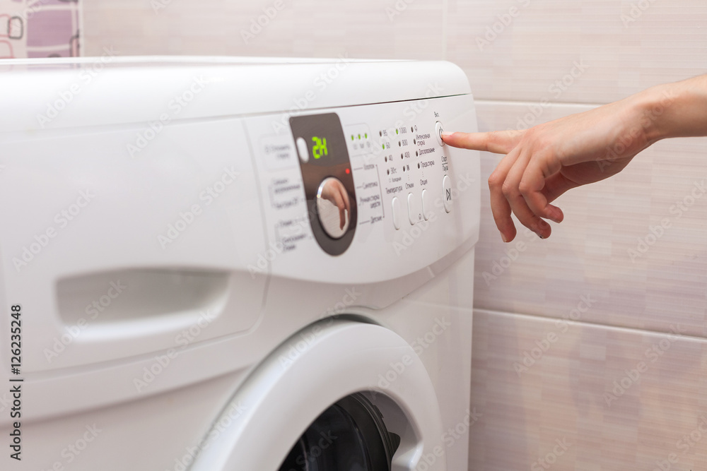 Young woman or housekeeper has a laundry day at home, she select the program Young woman or housekeeper has a laundry day at home, she select the program