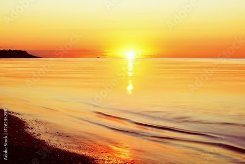 idealistic gentle morning seascape. Water pale orange flowers, because of the rising sun horizon. beautiful summer sea background. In the distance is the Cape. 