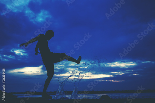 Fototapeta Naklejka Na Ścianę i Meble -  Silhouette of man who kicks the water at the lake. angry concept