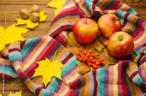 Striped scarf, red apples and maple leaves on a wooden table aut