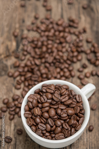 White coffee cup full of Roasted coffee beans on the old wood table background. (View from top)
