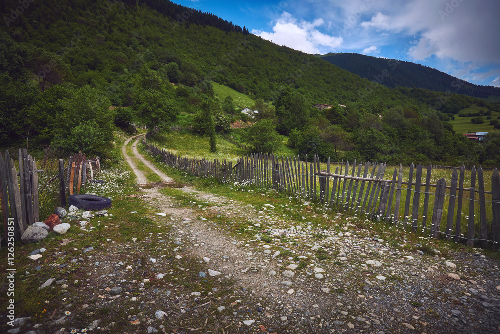 Грунтовая дорога вдоль забора в горной деревне в Сванетии, Грузия