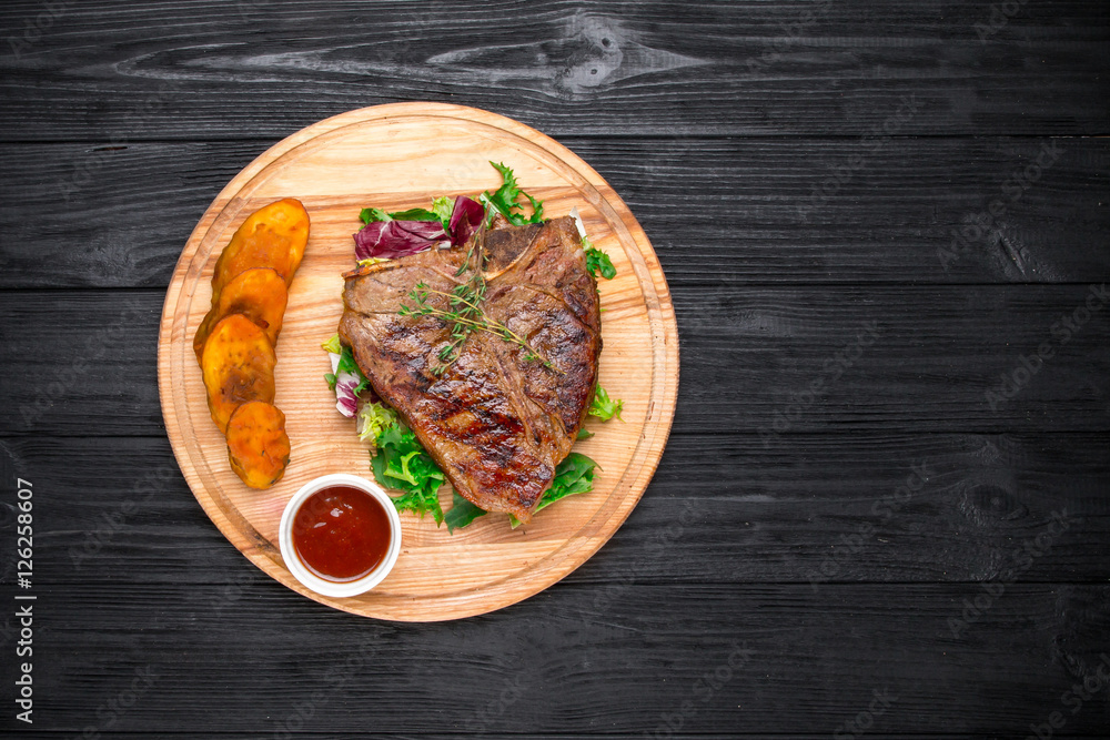 Grilled T-Bone Steak with seasoning and sauce on black wooden ba Grilled T-Bone Steak with seasoning and sauce on black wooden ba