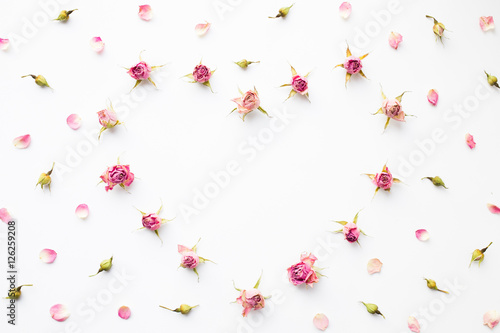 Background with shape of heart made of pink dry roses on white. Top view, flat lay, romantic card.