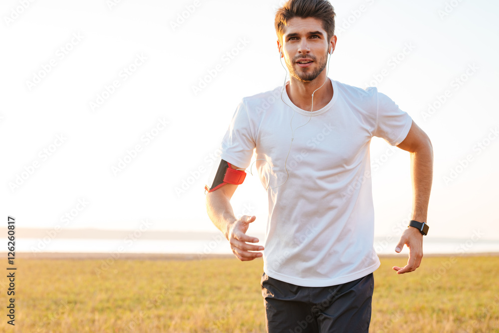 Fototapeta premium Handsome young sportsman running outdoors and listening to music