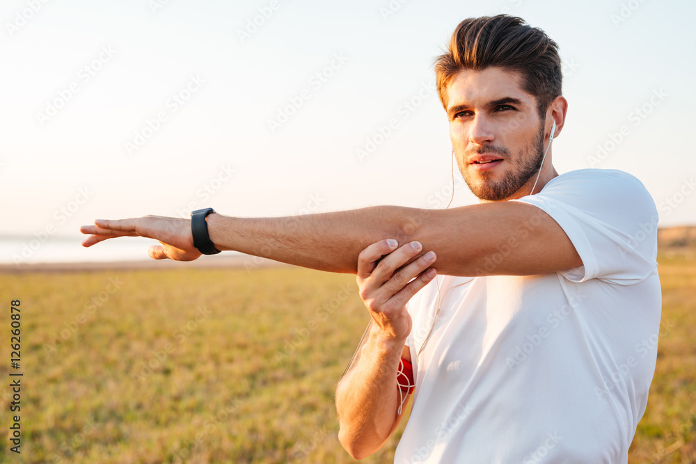 Φωτογραφία Concentrated sportsman stretching hands and listening to music with earphones
